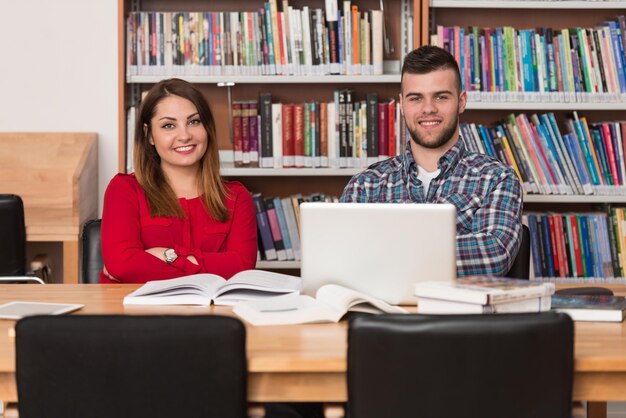 Dans la bibliothèque beau deux étudiants avec ordinateur portable et livres travaillant dans une bibliothèque universitaire de lycée faible profondeur de champ