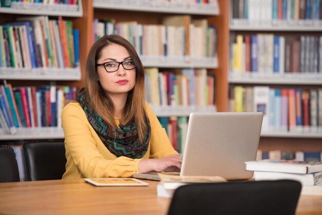 Dans la bibliothèque belle étudiante avec ordinateur portable et livres travaillant dans une bibliothèque universitaire de lycée faible profondeur de champ