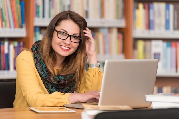 Dans la bibliothèque belle étudiante avec ordinateur portable et livres travaillant dans une bibliothèque universitaire de lycée faible profondeur de champ