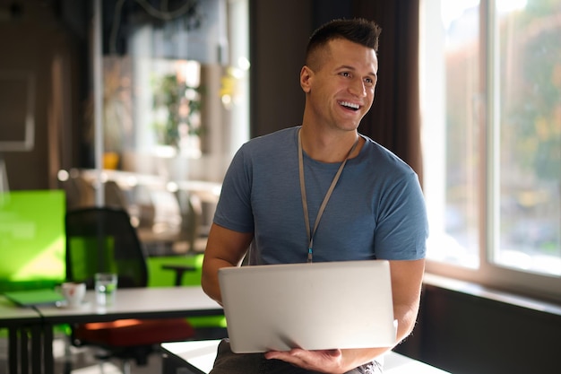 Dans le bureau. Jeune homme assis sur la table avec un ordinateur portable