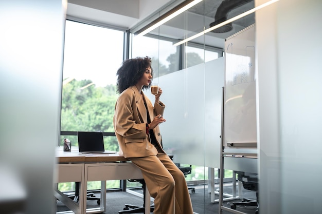 Dans le bureau. Jolie jeune femme aux cheveux bouclés en costume beige au bureau