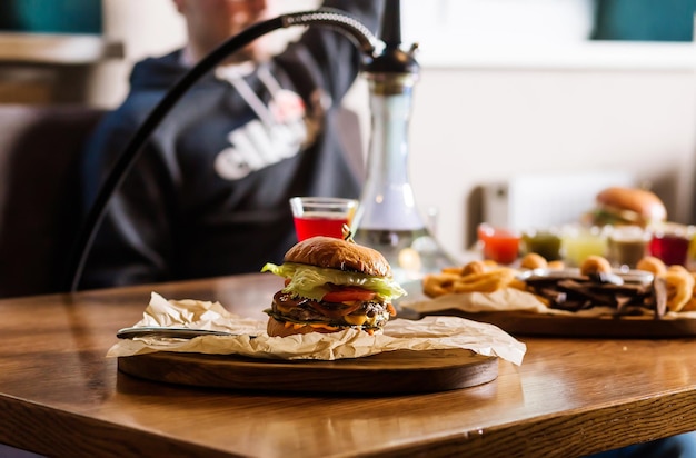 Dans un café à l'atmosphère chaleureuse, un ensemble de teintures d'alcool narguilé et une assiette en bois avec un hamburger sont assis sur la table