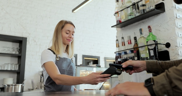 Dans le café, une femme prépare du café à emporter pour un client qui paie par téléphone portable sans contact au système de carte de crédit.