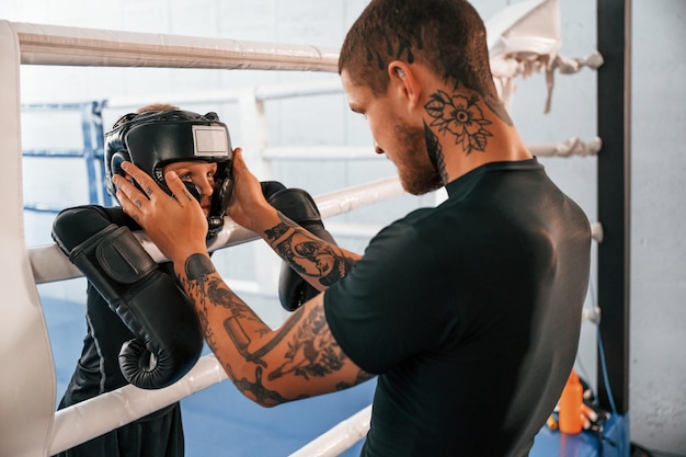 Photo dans un casque de protection et avec des lueurs sur le ring, l'entraîneur enseigne les techniques de boxe à l'intérieur