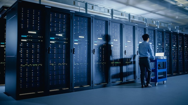 Dans le centre de données moderne, l'ingénieur informatique effectuant l'entretien et le diagnostic pousse le chariot à côté des supports de serveur Planification de la mise à jour et de la maintenance de l'équipement du système