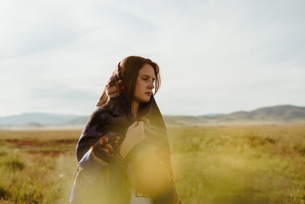 Dans le contexte de l'herbe de la steppe, il y a une fille triste avec une cape sur la tête et tient l'ac