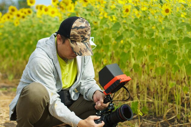 Dans les coulisses de la vidéo VDO prise de vue avec une caméra de cinéma numérique d'un homme asiatique des années 50 sous le soleil dans un champ de fleurs jaunes de tournesol sur une montagne de ciel bleu à des poses féminines dans un paysage extérieur