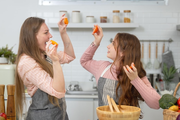 Dans une cuisine moderne et impeccable, une mère et sa fille souriantes montrent comment préparer des légumes à la tomate pour le dîner