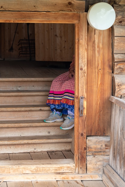 Dans les escaliers de la hutte se trouve une grand-mère vêtue de style folklorique russe et de baskets modernes