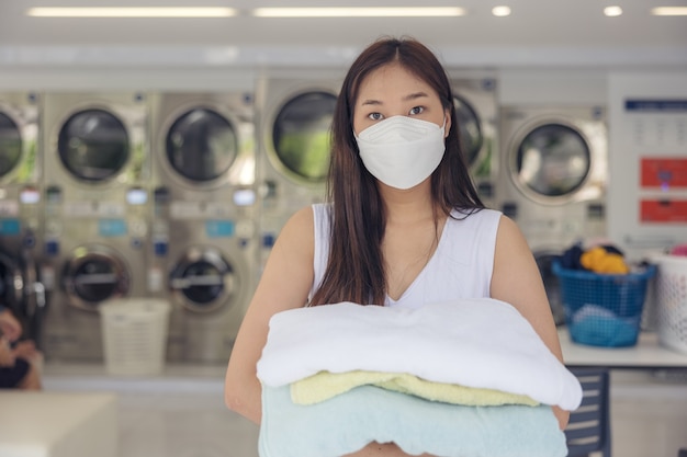 Dans la laverie en libre-service avec des machines à sécher en toile de fond, une jeune femme savoure des vêtements propres et repassés.