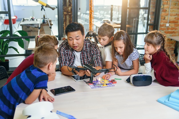 Photo dans une leçon de physique et de mécanique, un jeune enseignant asiatique montre un quadcopter pour des élèves caucasiens en classe dans une école intelligente moderne. science, drone, ingénierie et concept futur.