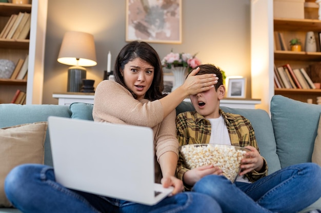 Dans leur salon, une mère et son fils partagent une soirée de cinéma passionnante avec du pop-corn à la main, ils regardent un film choquant sur l'ordinateur portable, la mère couvrant les yeux de son fils avec sa main.