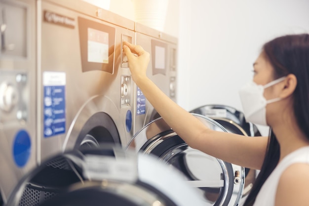 Photo dans un magasin de blanchisserie avec de nombreuses machines à laver automatiques, une femme portant un masque fait la lessive.