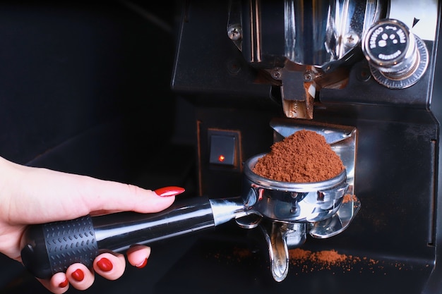 Dans la main féminine se trouve un porte-café, les grains de café sont versés dans le filtre