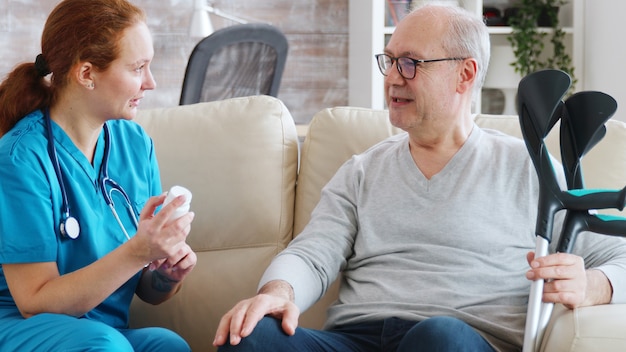 Dans une maison de retraite, une infirmière parle avec un homme âgé du dosage des médicaments. Aide-soignante et assistante sociale