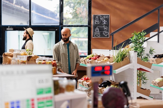 Dans un marché respectueux de l'environnement, un homme arabe navigue dans les allées en se concentrant sur l'achat d'épiceries durables. Un client masculin soutient les petites entreprises locales et achète des produits biologiques frais.