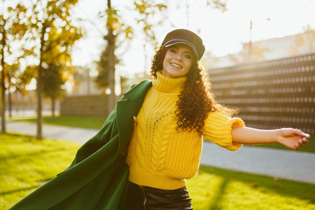 Dans le parc d'automne fille tourbillonnante dans un pull jaune vif jetant sur l'épaule un manteau vert