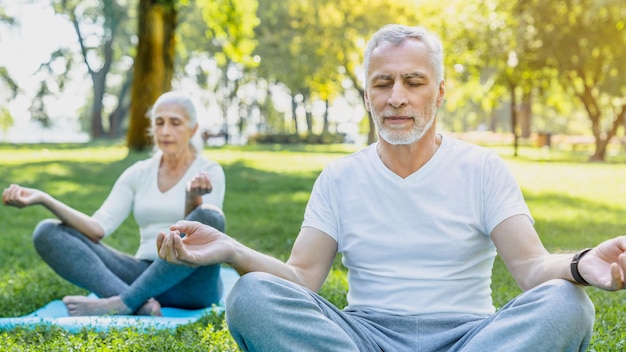 Photo dans le parc de yoga, un couple âgé assis dans une pose de lotus sur l'herbe verte dans le calme et la méditation.