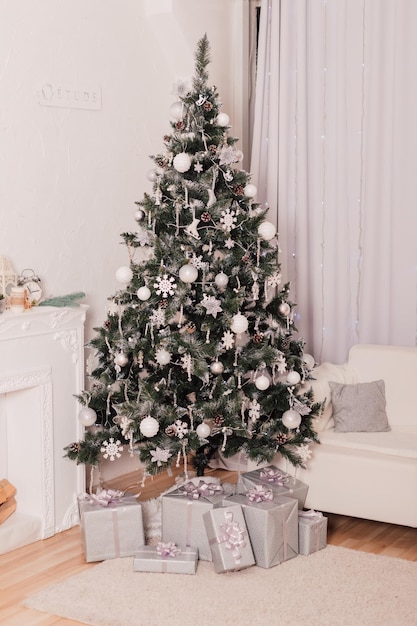 Dans une pièce lumineuse avec un canapé blanc il y a un sapin de Noël vert décoré de décor blanc