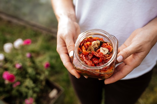 Dans sa main se trouve un pot ouvert de tomates séchées au soleil avec de l'huile d'olive.