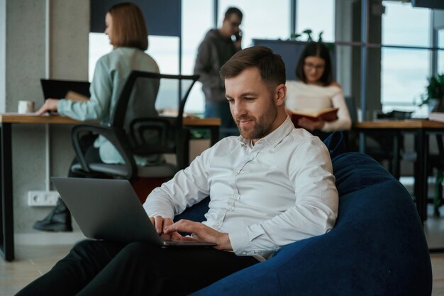 Dans le sac à haricots bleu avec l'ordinateur portable Les gens travaillent au bureau