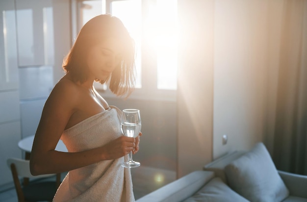 Dans une serviette blanche, la jeune femme est à l'intérieur dans la chambre d'une maison moderne pendant la journée