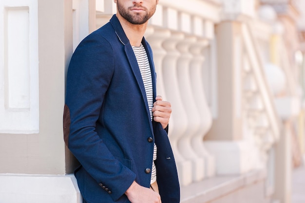 Dans son propre style parfait. Image recadrée d'un beau jeune homme à lunettes et veste intelligente en détournant les yeux tout en se tenant à l'extérieur