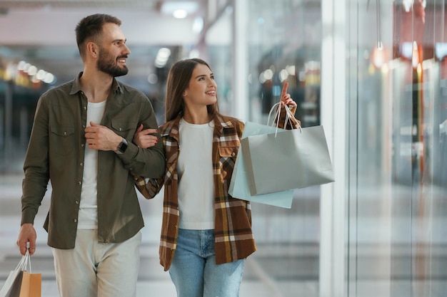 Dans des vêtements décontractés avec des sacs de shopping Un jeune couple est au supermarché ensemble