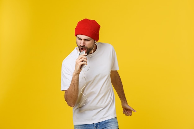 Danse. Beau jeune homme élégant dans des écouteurs tenant un téléphone portable et dansant en se tenant debout contre le jaune.