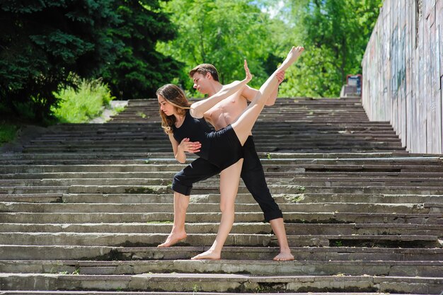 Danse contemporaine Homme et femme en danse passionnée pose dans le parc Jeune couple dansant la danse moderne Fille faisant le grand écart Homme au torse nu Vieux escaliers dans les arbres du parc en arrière-plan