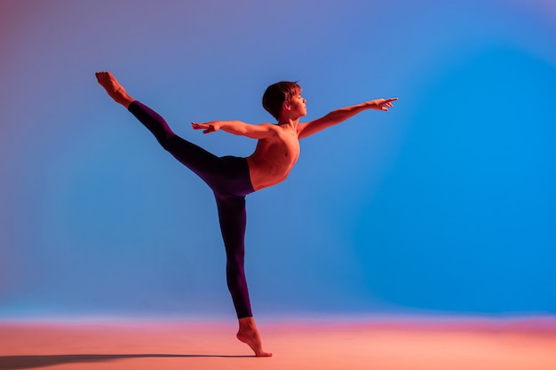 Danseur de ballet adolescent danse pieds nus sous une lumière colorée.