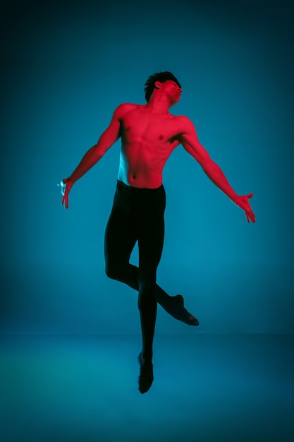 Le danseur de ballet athlétique masculin exécutant la danse sur fond bleu vif. Prise de vue en studio. Ballet moderne, concept contemporain. Fit jeune homme. modèle caucasien