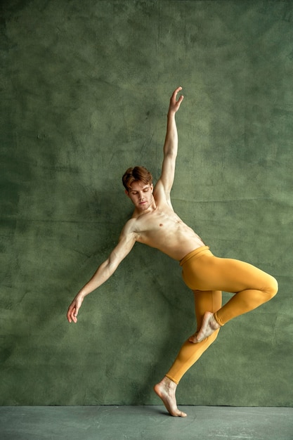 Le danseur de ballet masculin pose au mur de grunge dans le studio de danse. Interprète au corps musclé, grâce et élégance des mouvements