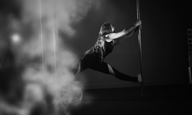 Le danseur sur le pylône en studio. Fille faisant des exercices sur un équipement sportif.