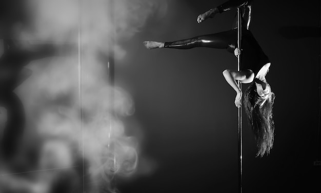 Le danseur sur le pylône en studio. Fille faisant des exercices sur un équipement sportif.