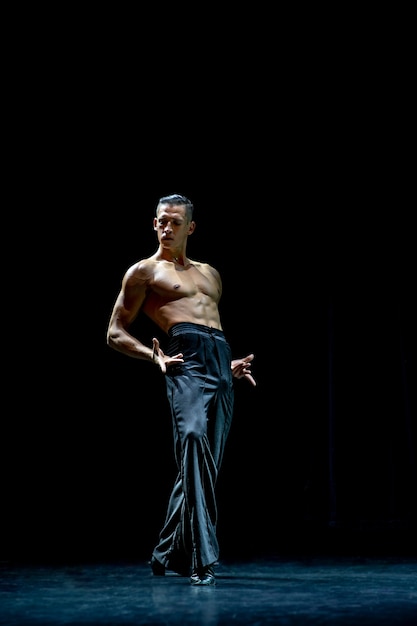 Danseur de salon musculaire seins nus faisant pose isolé sur fond noir.