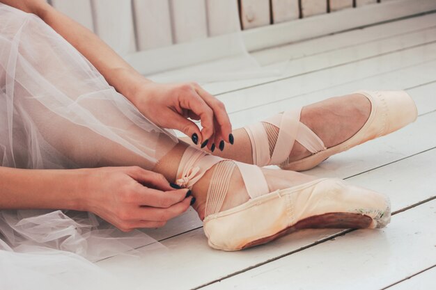 Les danseurs de ballet authentiques ballerine assis sur le sol et attachant des chaussures de pointe, gros plan