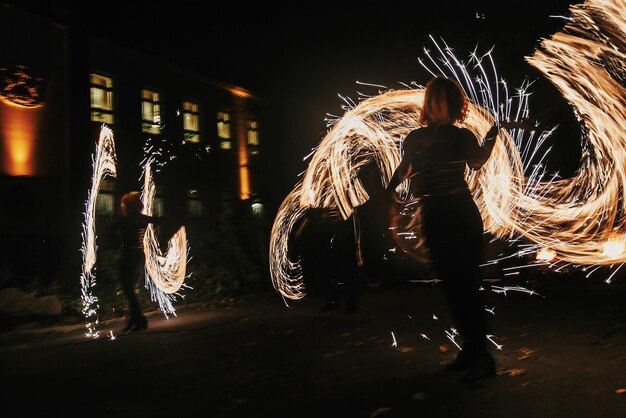 Les danseurs de feu balancent le feu tournant et l'homme jongle avec des étincelles lumineuses dans la nuit spectacle de feu spectacle et divertissement spectacle de feu incroyable la nuit au festival ou à la fête de mariage