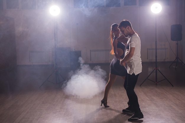 Des danseurs habiles se produisant dans la pièce sombre sous la lumière et la fumée du concert. Couple sensuel exécutant une danse contemporaine artistique et émotionnelle.
