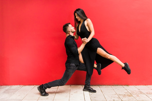 Photo danseurs de rue effectuant le tango contre le mur lumineux rouge