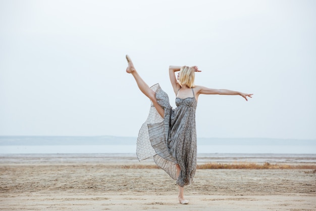 Danseuse gracieuse de la jeune femme en belle robe dansant sur la plage