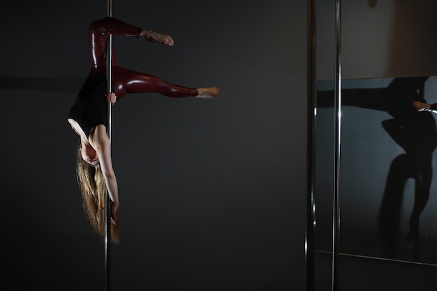 La danseuse sur le pylône dans le studio Fille faisant des exercices sur un équipement sportif