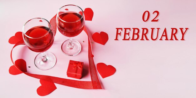 Date du calendrier sur fond clair avec deux verres de vin rouge coffret cadeau rouge et coeurs 2 février