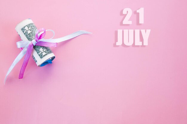 Date du calendrier sur fond rose avec des billets d'un dollar enroulés épinglés par un ruban rose et bleu le 21 juillet