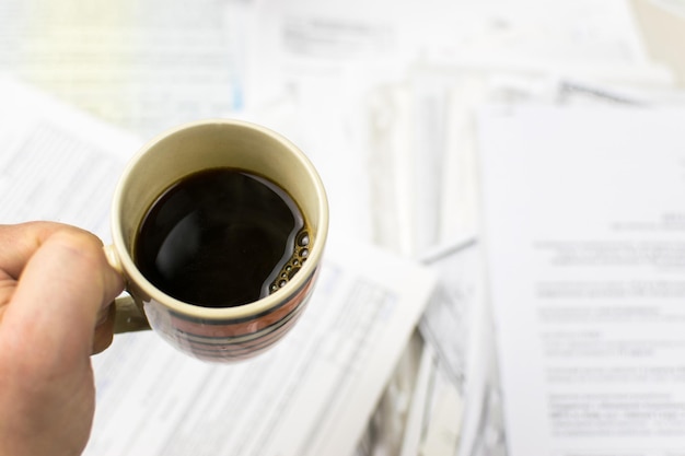 Date limite écrite sur papier et une tasse de café à la main sur fond de papiers éparpillés