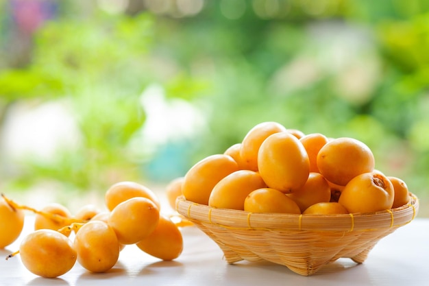 Dates jaunes fraîches dans un panier en bois sur une table blanche avec fond naturel flou