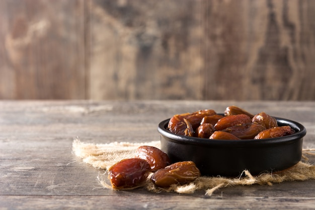 Dates de nourriture dans un bol noir sur l'espace de copie de table en bois