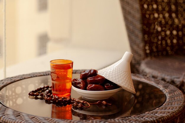 Photo des dattes dans une assiette en verre avec un couvercle une boisson orientale et un chapelet sur un verre