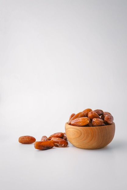 Des dattes entières dans un bol rond en bois avec des dattes éparpillées sur un fond blanc propre Concept d'alimentation saine minimaliste avec des fruits secs naturels