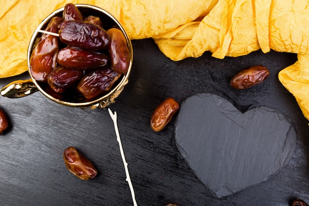 Dattes de fruits secs dans une tasse dorée près de coeur noir ardoise